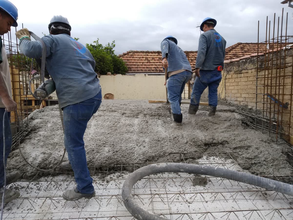 Equipe concretando laje com lançamento por mangote, espalhando e sarrafeando o concreto sobre a armação